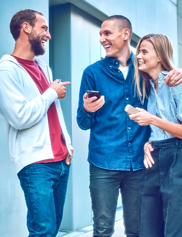 شخصان يحملان جهازي IQOS ILUMA يبتسمان بينما تنظر صديقتهما إلى تطبيق IQOS على هاتفها المحمول.